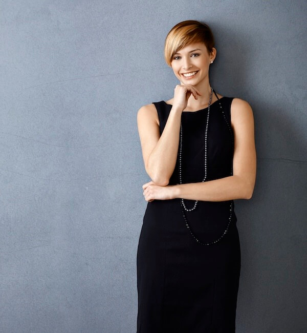 A smiling woman in a long, black dress with short hair